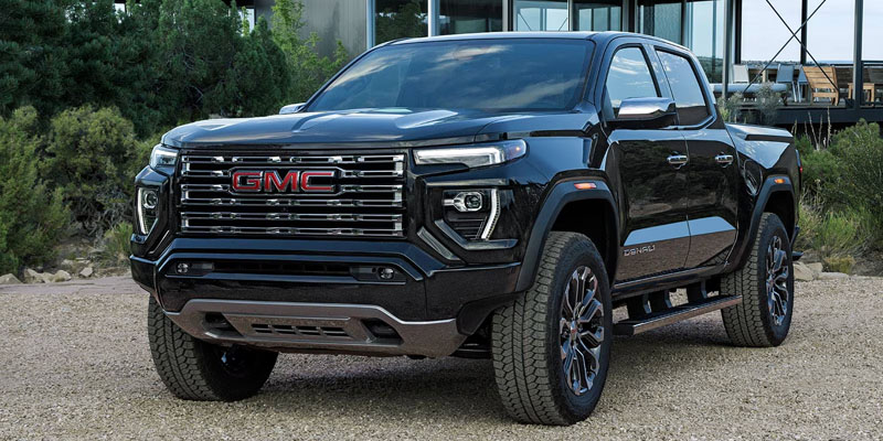 A black GMC truck parked on a gravel surface in front of a modern building.