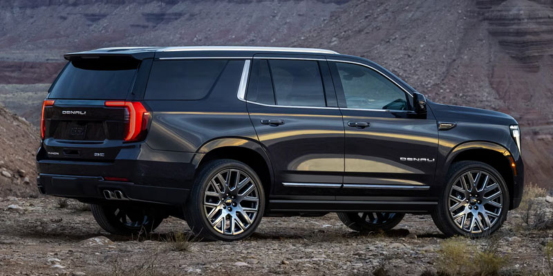 A dark metallic GMC Yukon Denali parked on a rocky, desert terrain with steep canyon walls in the background.