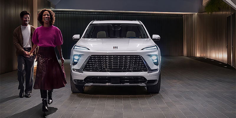 A white Buick SUV parked inside a modern covered driveway while a smiling couple walks past in the foreground.